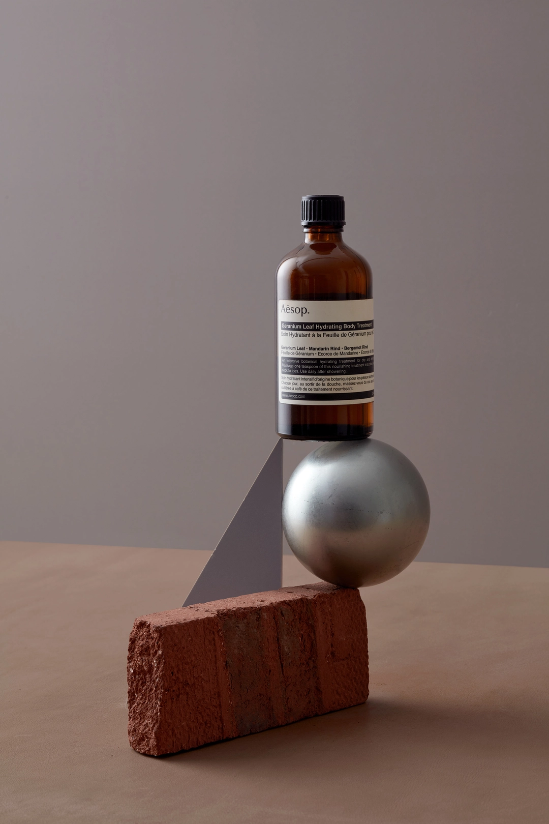 Aesop bottle balanced on silver ball and brick still life