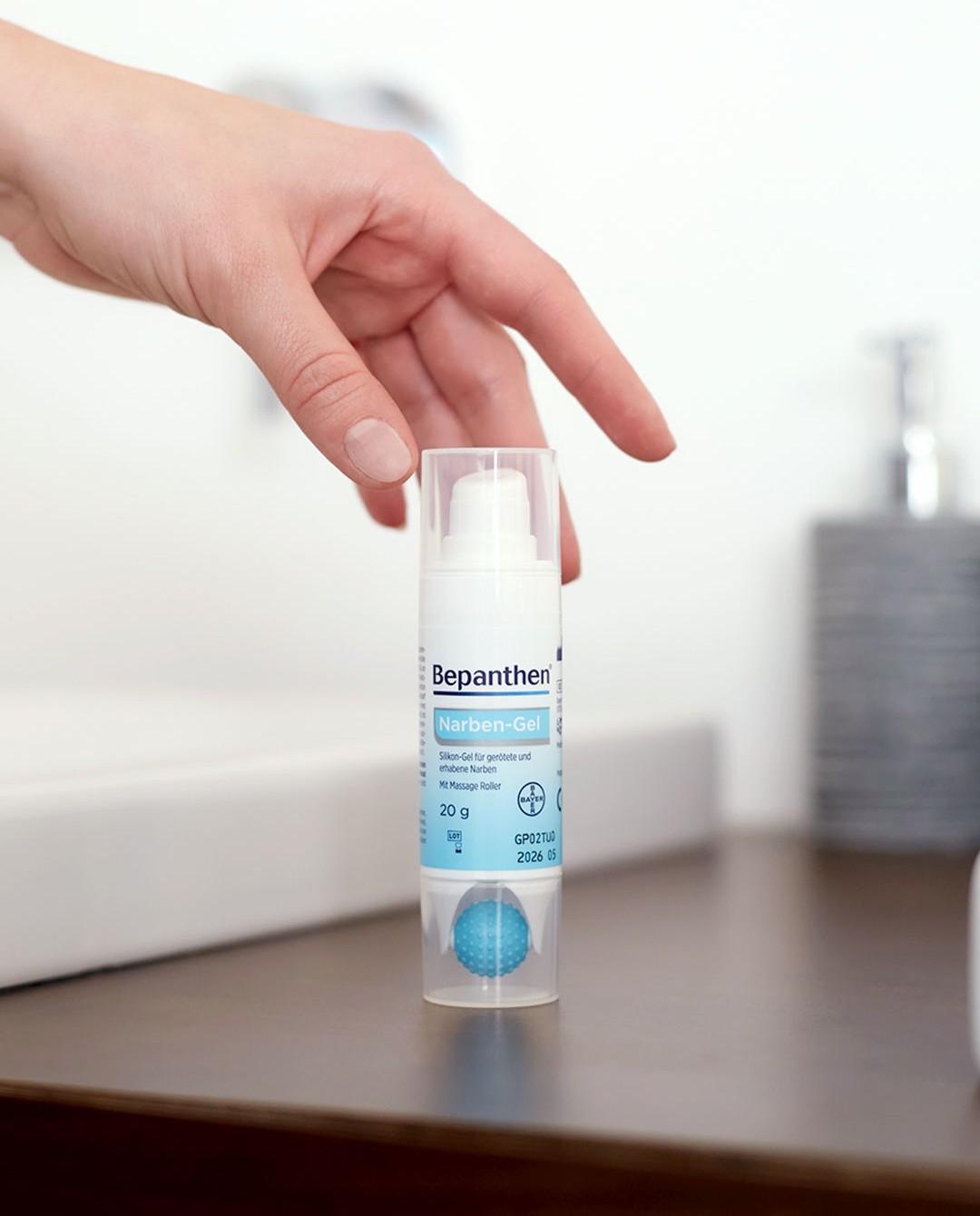 Bepanthen Narben-Gel on a bathroom counter, a hand reaching for it