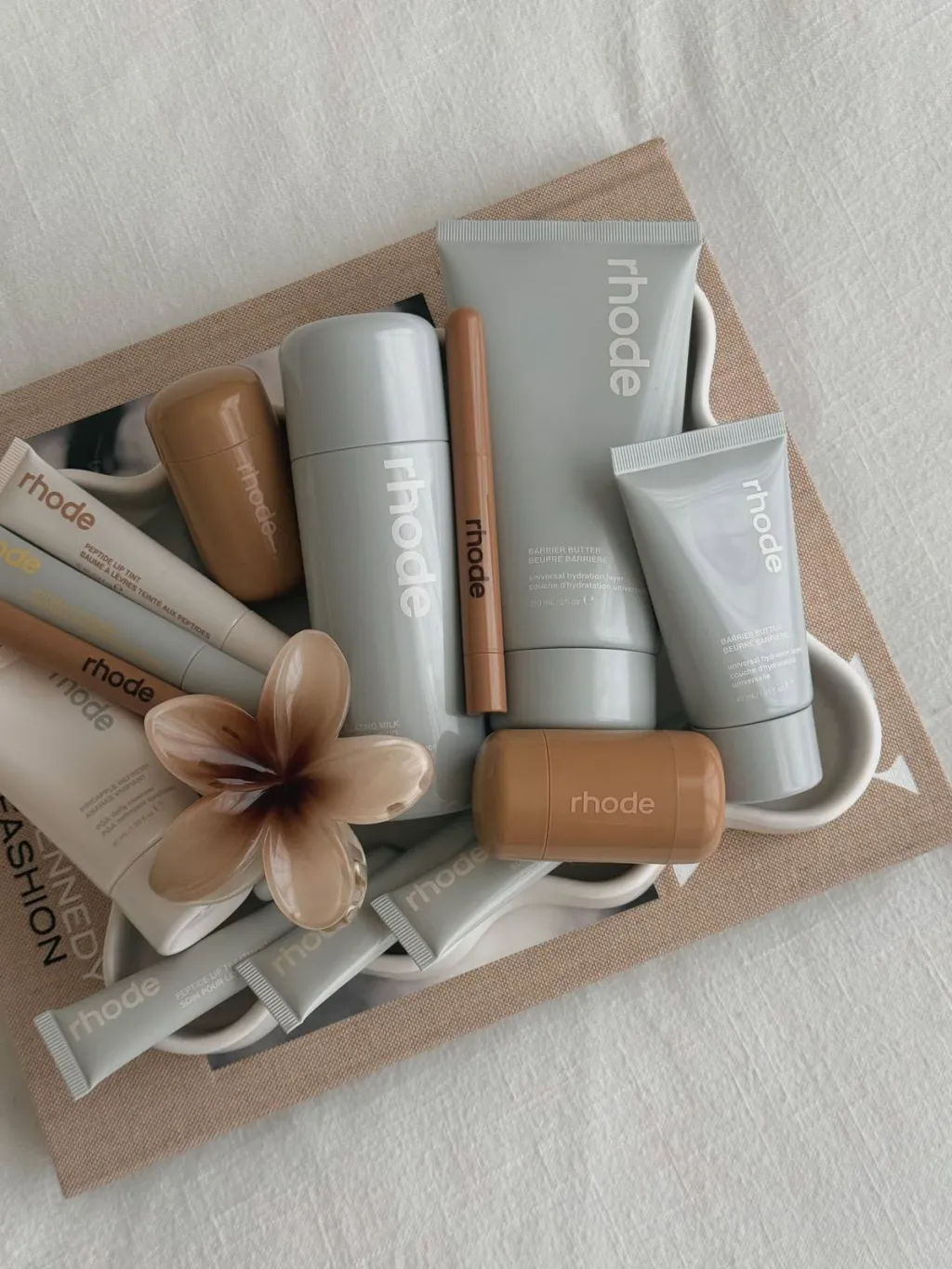 rhode product flatlay on linen with frangipani