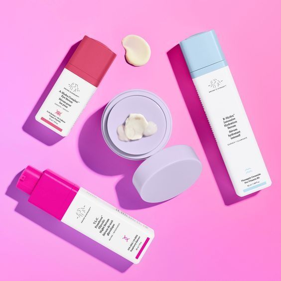 Drunk Elephant flatlay on hot pink, A-Gloei Marula oil, B-Hydra serum and T.L.C. Framboos arranged with cream samples
