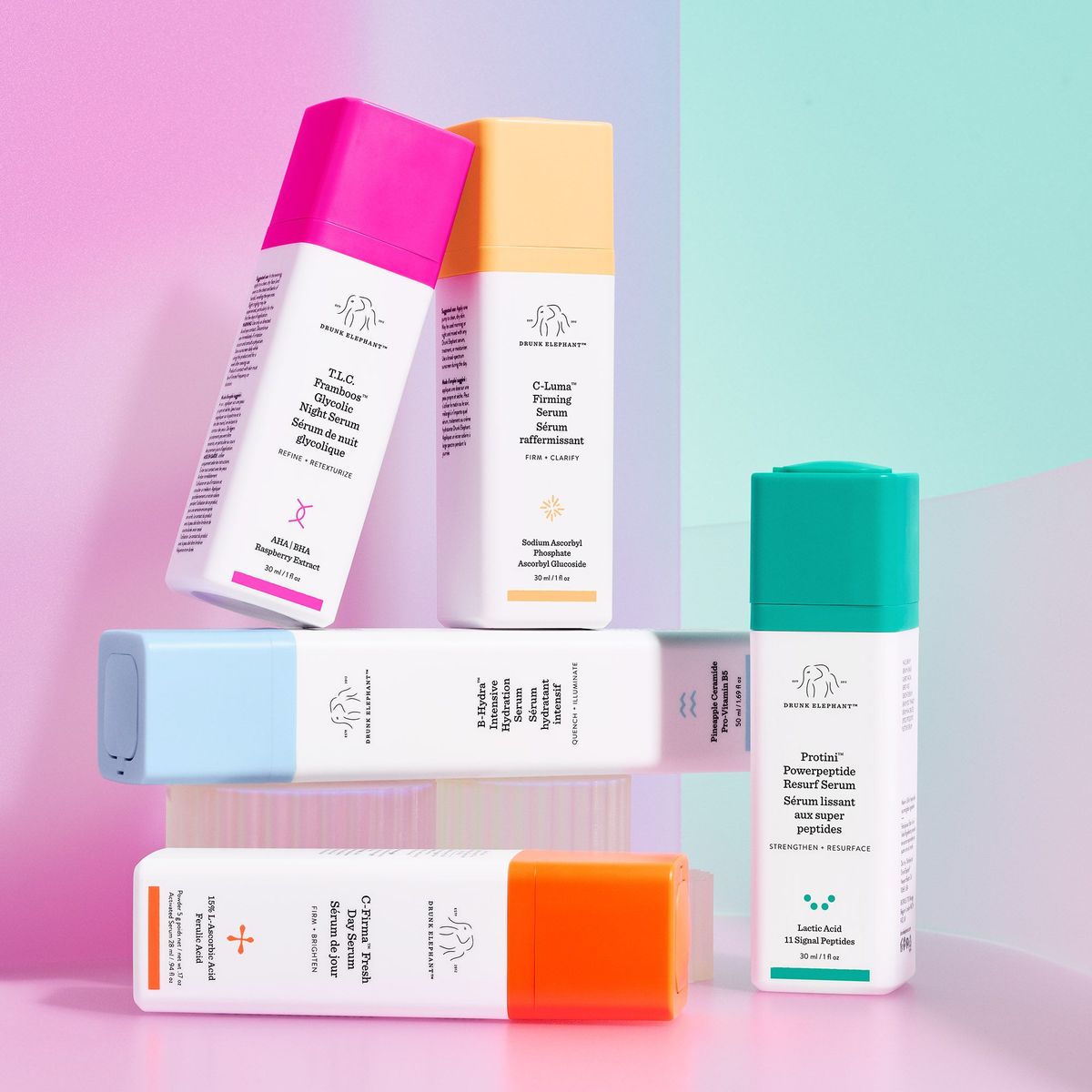 Drunk Elephant serum family stack, T.L.C. Framboos, C-Luma, B-Hydra, C-Firma and Protini on a pastel pink and green surface