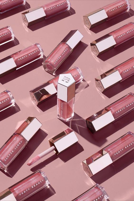 Fenty Beauty Gloss Bomb in arrangement on dusty rose, editorial flatlay