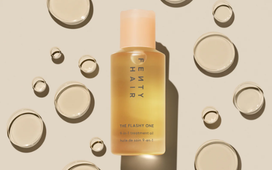 Fenty Hair The Flashy One 9-in-1 treatment oil, bottle on beige with oil droplets