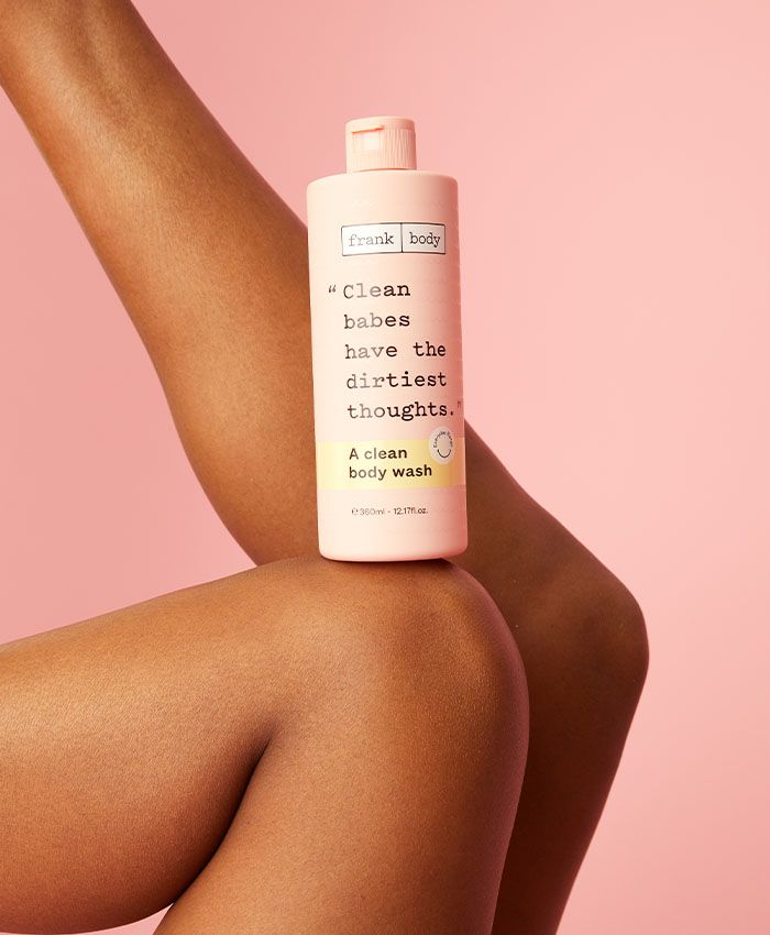 Frank Body Clean Body Wash perched on a model's leg, pink studio