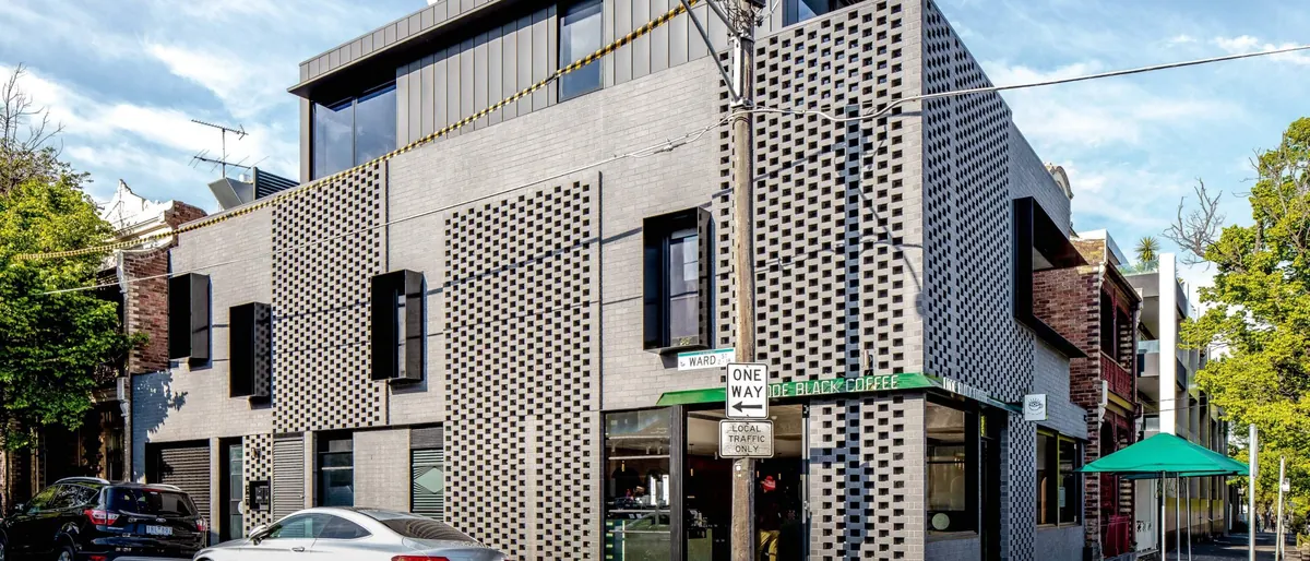 The building from the street: grey brick with perforated brick screens and a dark metal top floor