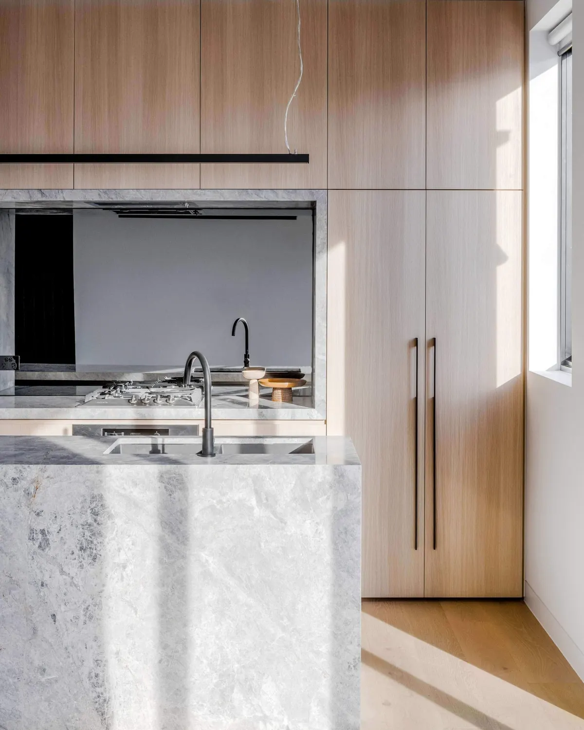 Marble kitchen island in front of full-height oak joinery and a mirrored splashback