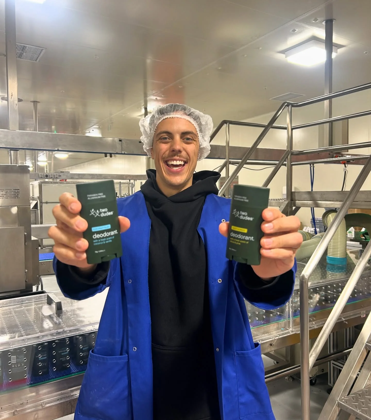 Two Dudes co-founder on the New Zealand factory floor holding deodorant cartons